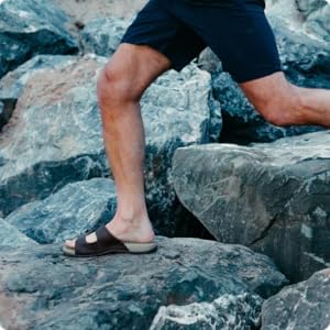 person wearing brown sandals jumping between rocks